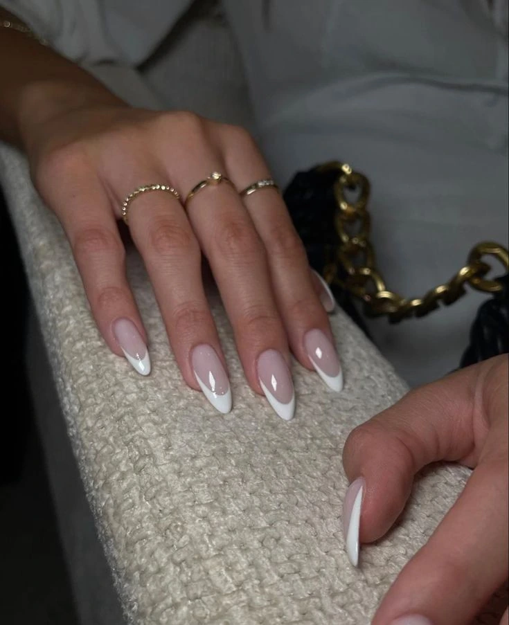 Classic white French tips in Shellak on almond-shaped nails with gold rings