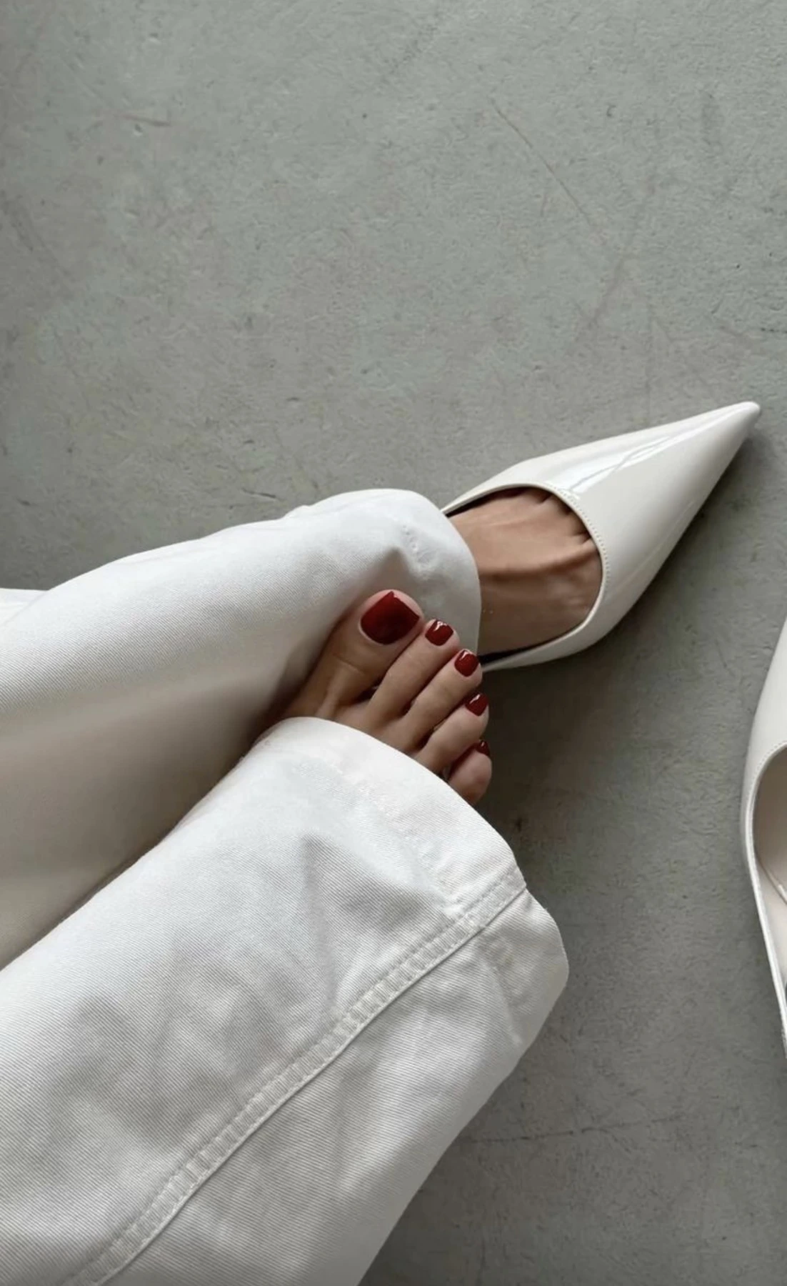 Deep red pedicure with white trousers and pointed shoes