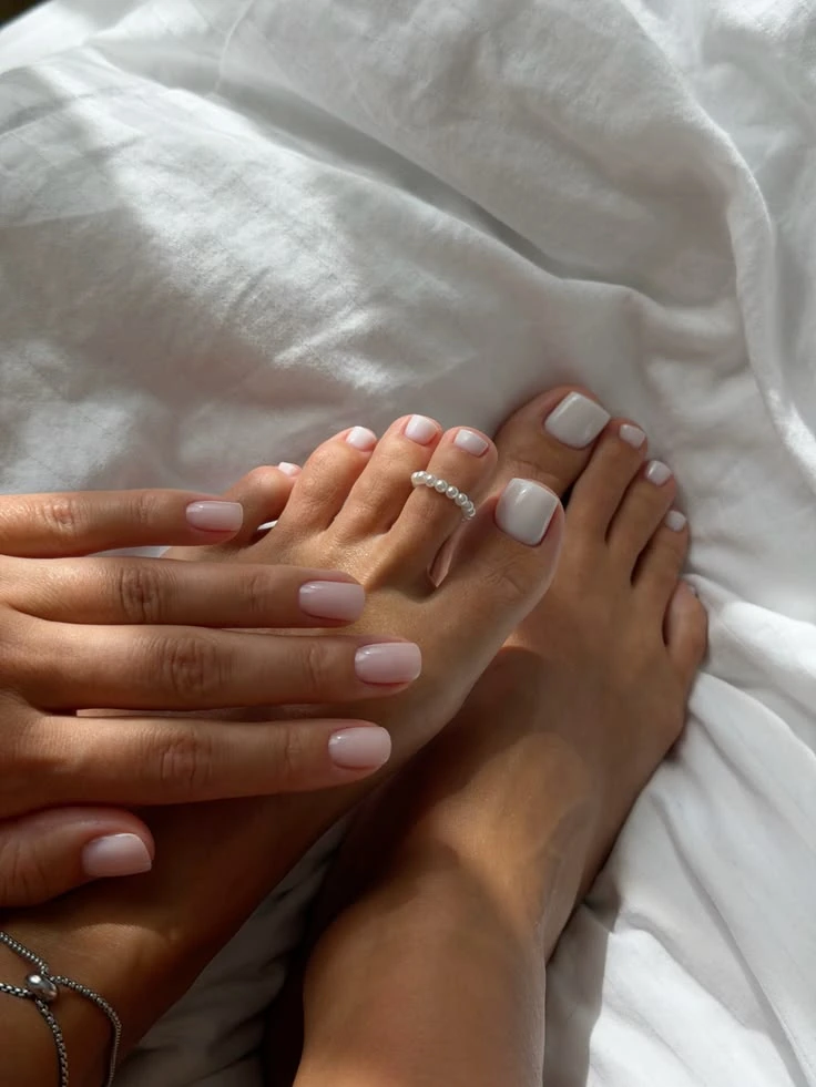 Matching soft pink manicure and pedicure on white bedding