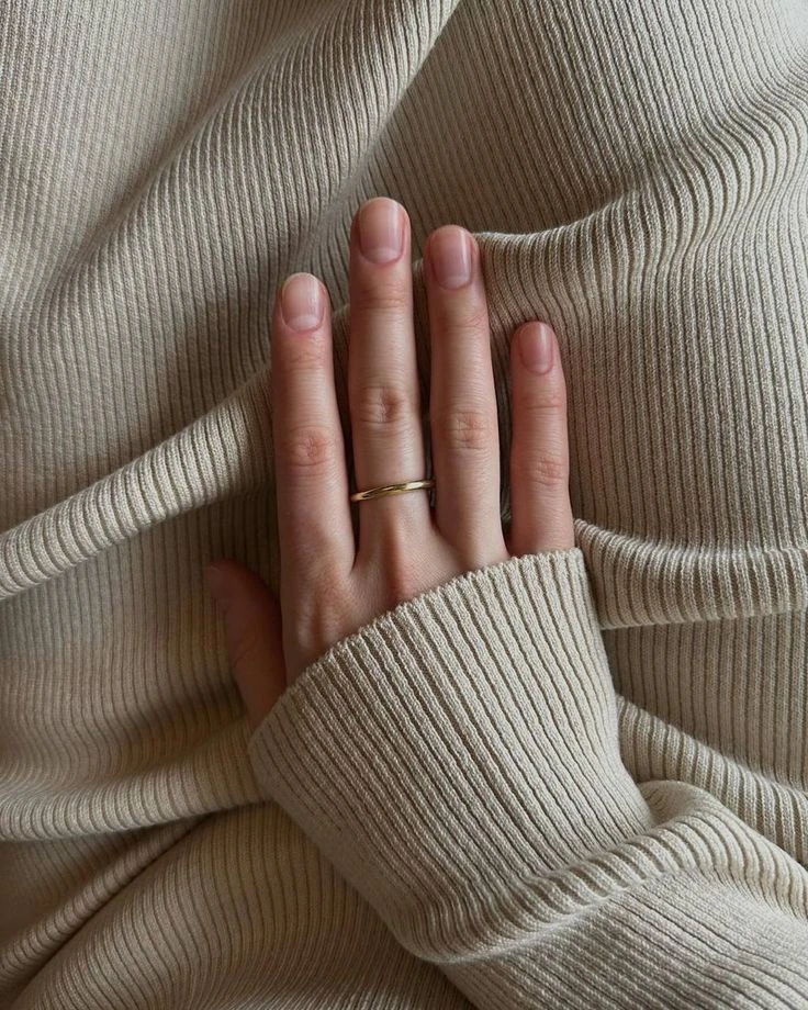 Short natural manicure with a thin gold ring on a cream ribbed knit