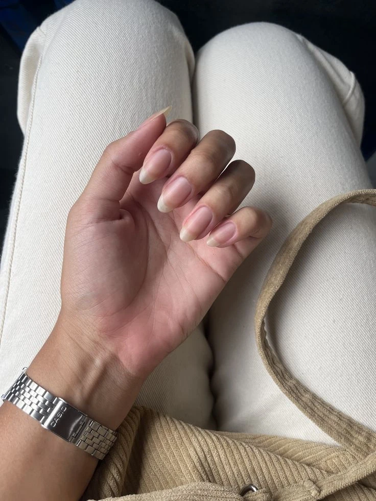 Long natural almond nails with a silver watch and cream corduroy